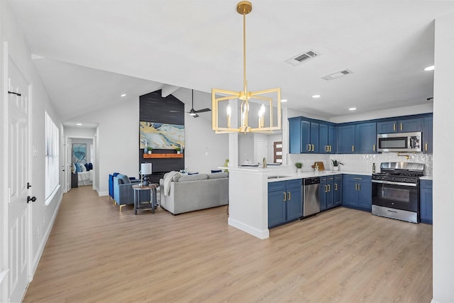 kitchen featuring appliances with stainless steel finishes, backsplash, light wood-type flooring, hanging light fixtures, and vaulted ceiling