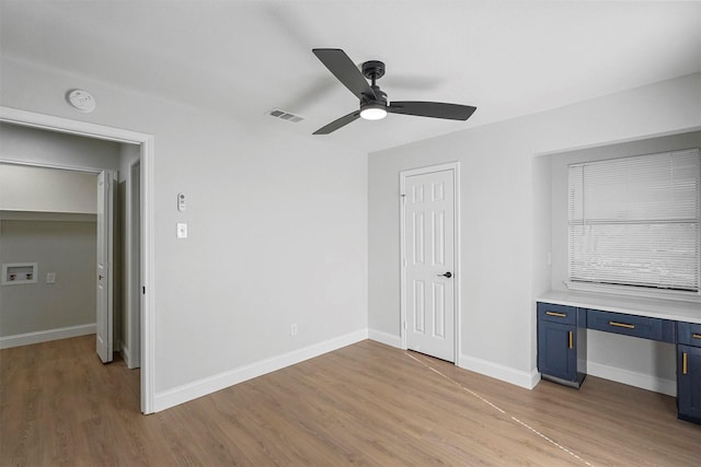 unfurnished bedroom with ceiling fan, built in desk, and light hardwood / wood-style floors