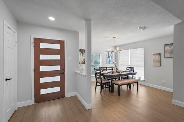 foyer entrance with light wood-type flooring, an inviting chandelier, and a textured ceiling