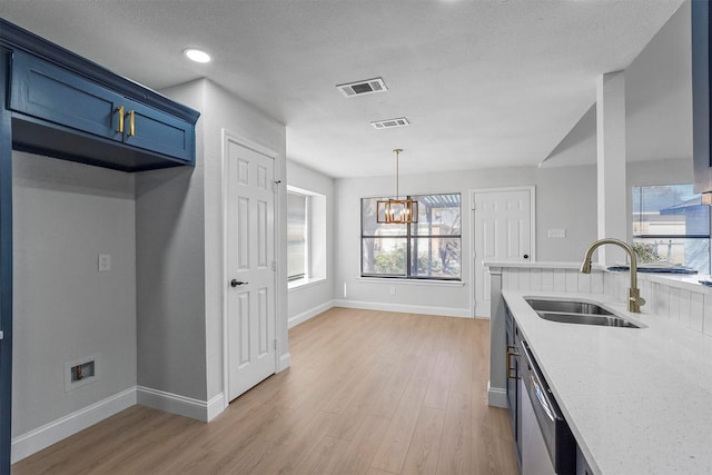 kitchen featuring stainless steel dishwasher, sink, light wood-type flooring, light stone counters, and a chandelier