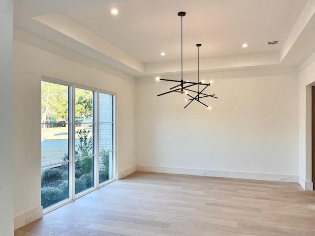 empty room featuring a raised ceiling, an inviting chandelier, and light hardwood / wood-style flooring