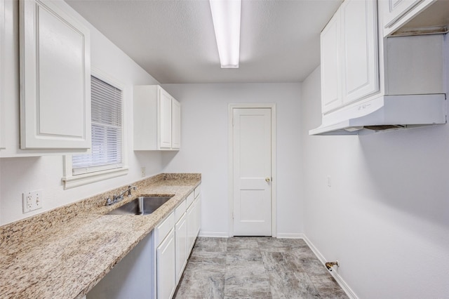 kitchen featuring light stone counters, sink, and white cabinets