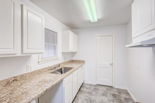 kitchen featuring white cabinets, light stone counters, and sink