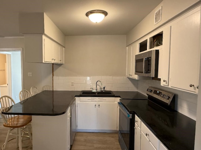 kitchen with stainless steel appliances, dark countertops, white cabinets, a sink, and a peninsula