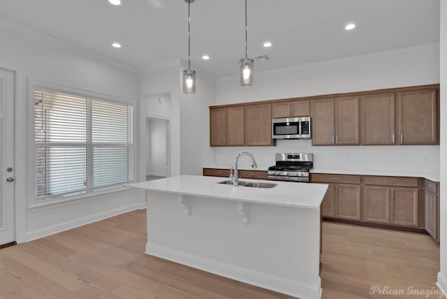 kitchen with appliances with stainless steel finishes, a kitchen island with sink, decorative light fixtures, ornamental molding, and sink