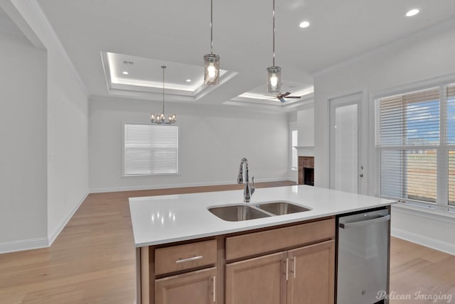 kitchen with an island with sink, a brick fireplace, stainless steel dishwasher, ceiling fan with notable chandelier, and sink