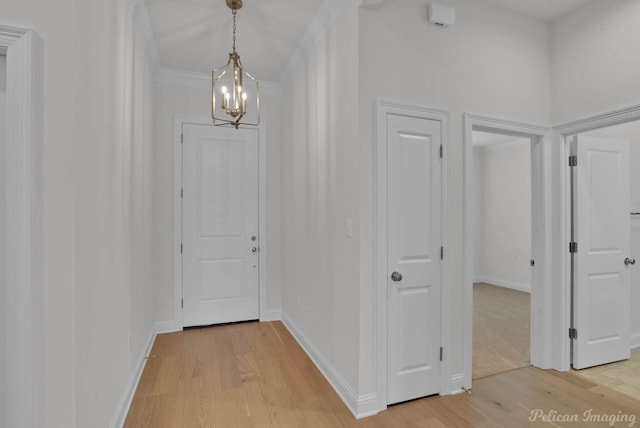 hallway with an inviting chandelier, ornamental molding, and light hardwood / wood-style flooring