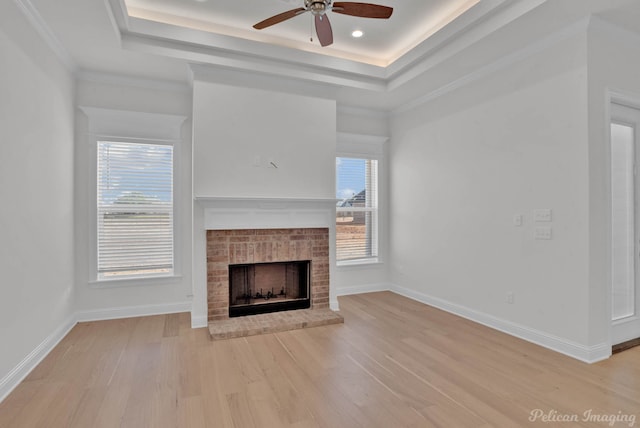 unfurnished living room with ceiling fan, a fireplace, a tray ceiling, and light hardwood / wood-style floors