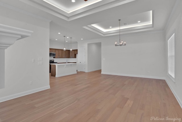 unfurnished living room with a raised ceiling, a notable chandelier, and light wood-type flooring