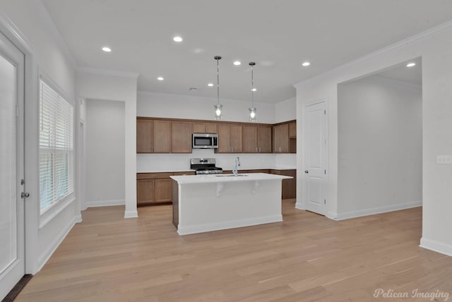 kitchen featuring light hardwood / wood-style floors, hanging light fixtures, appliances with stainless steel finishes, and a kitchen island with sink