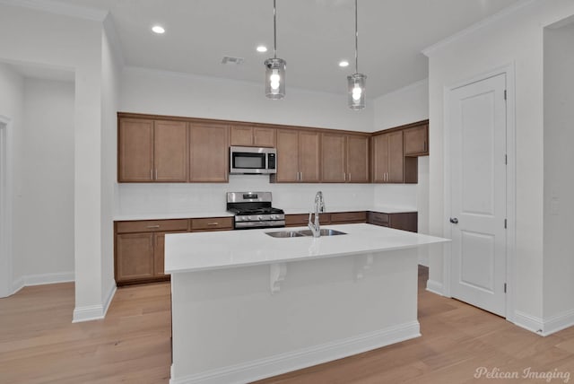 kitchen featuring stainless steel appliances, sink, hanging light fixtures, a kitchen island with sink, and light hardwood / wood-style flooring