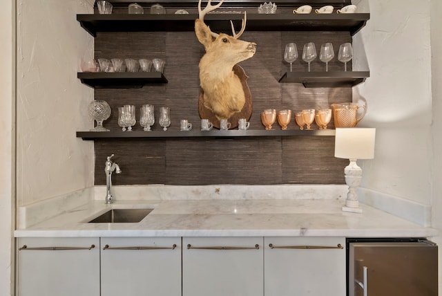 bar with light stone counters, sink, and white cabinetry