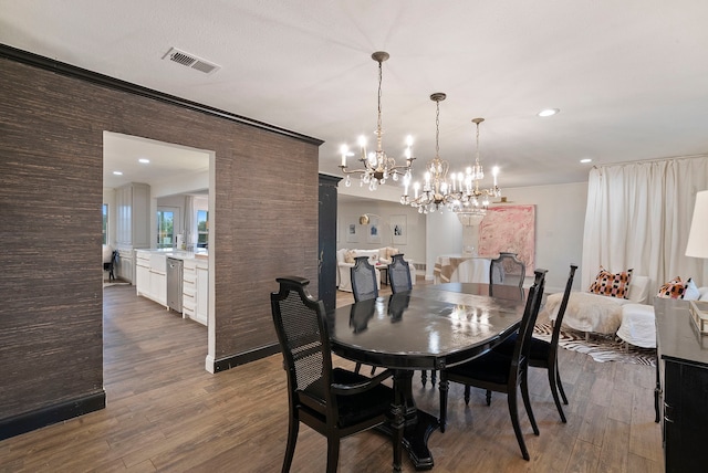 dining area featuring wood-type flooring, ornamental molding, and an inviting chandelier