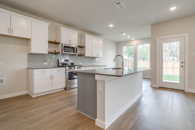 kitchen with appliances with stainless steel finishes, white cabinetry, sink, decorative backsplash, and a kitchen island with sink