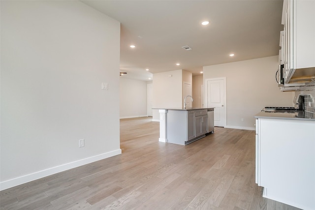 kitchen featuring an island with sink, appliances with stainless steel finishes, white cabinets, and light hardwood / wood-style flooring