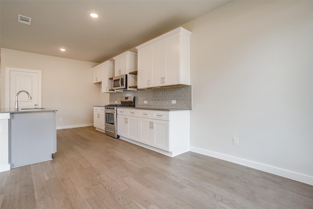 kitchen with sink, light hardwood / wood-style flooring, appliances with stainless steel finishes, backsplash, and white cabinets