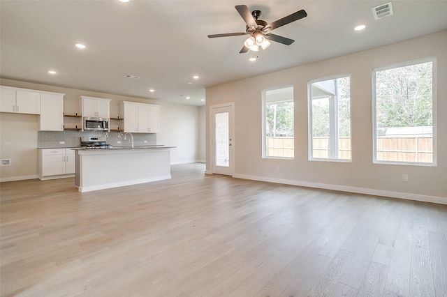 kitchen with white cabinetry, backsplash, a kitchen island with sink, stainless steel appliances, and light hardwood / wood-style floors