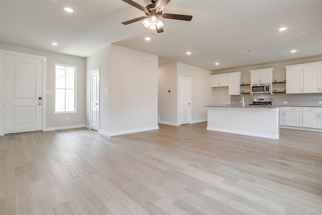 interior space featuring a center island with sink, light hardwood / wood-style floors, white cabinets, and appliances with stainless steel finishes