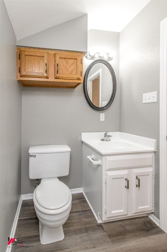 bathroom with toilet, lofted ceiling, wood-type flooring, and vanity