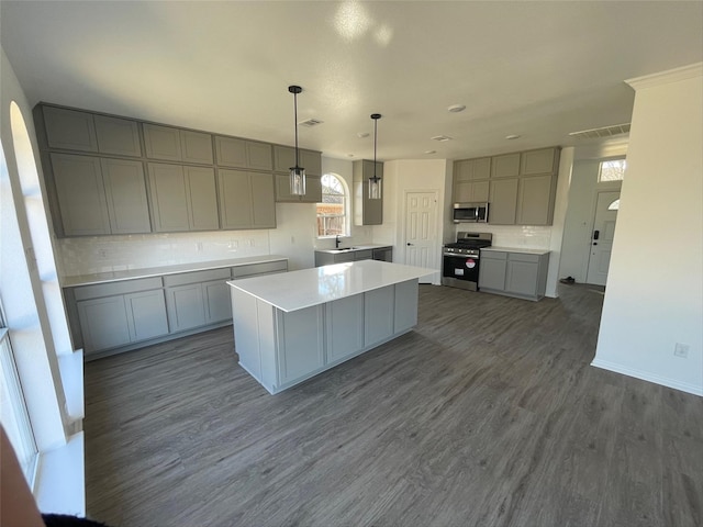 kitchen with a kitchen island, stainless steel appliances, hanging light fixtures, dark hardwood / wood-style floors, and gray cabinetry