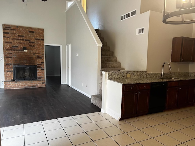 kitchen featuring a high ceiling, light tile patterned flooring, dishwasher, light stone counters, and sink