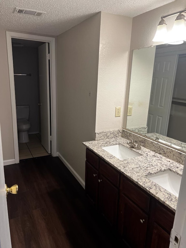 bathroom featuring toilet, a textured ceiling, wood-type flooring, and vanity