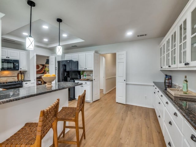 kitchen with light hardwood / wood-style floors, a raised ceiling, hanging light fixtures, white cabinets, and black appliances