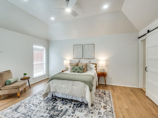 bedroom featuring light wood-type flooring, ceiling fan, lofted ceiling, and a barn door