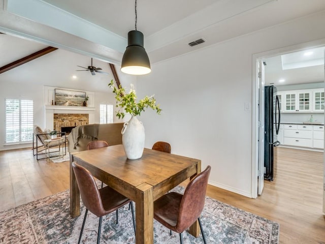 dining area with ceiling fan, vaulted ceiling with beams, and light wood-type flooring