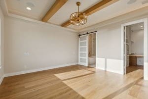 empty room with wood-type flooring, beamed ceiling, ornamental molding, and a barn door