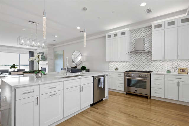 kitchen with decorative light fixtures, sink, white cabinetry, appliances with stainless steel finishes, and wall chimney exhaust hood