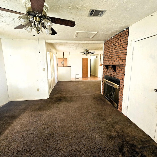 unfurnished living room featuring ceiling fan, a fireplace, a textured ceiling, and dark colored carpet