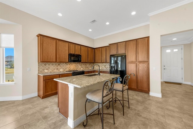 kitchen featuring light stone countertops, black appliances, a kitchen bar, sink, and a center island with sink