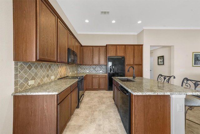 kitchen with a kitchen bar, a kitchen island with sink, light stone countertops, ornamental molding, and black appliances