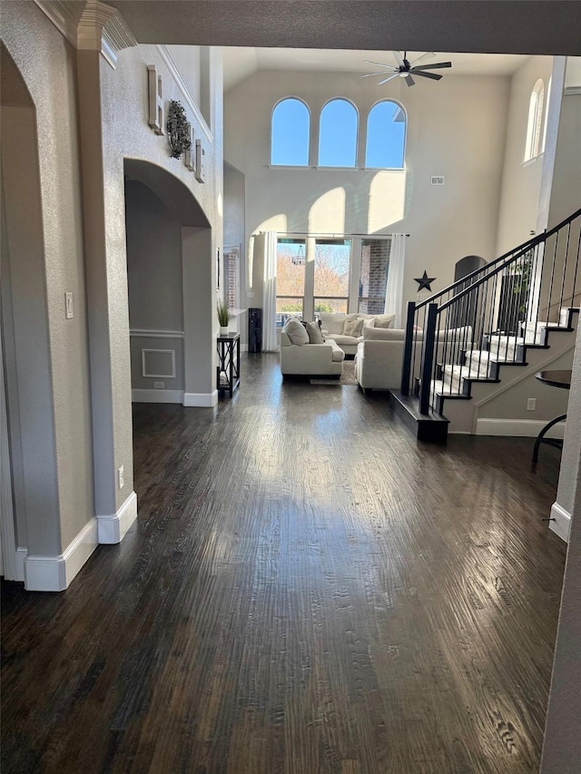 living room with ceiling fan, dark wood-type flooring, and a high ceiling