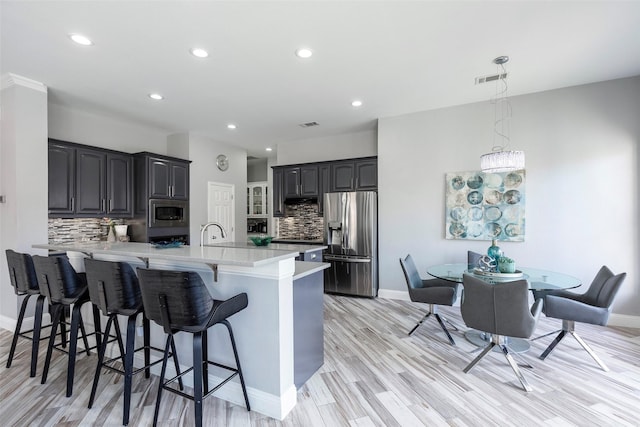 kitchen featuring appliances with stainless steel finishes, a kitchen breakfast bar, tasteful backsplash, light hardwood / wood-style floors, and kitchen peninsula