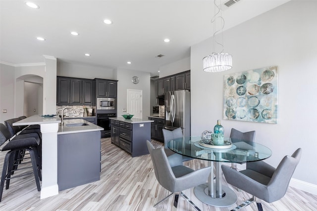 kitchen featuring pendant lighting, sink, backsplash, stainless steel appliances, and a center island with sink