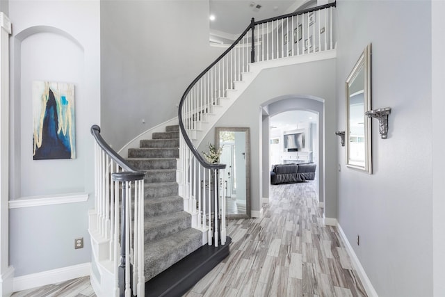 entryway featuring baseboards, stairs, a towering ceiling, wood finished floors, and arched walkways