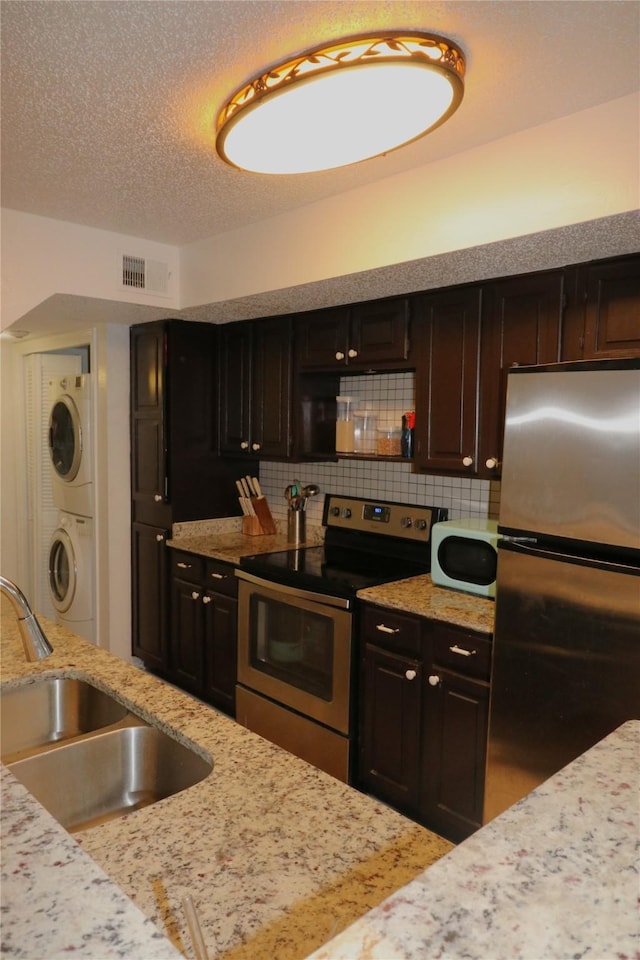 kitchen with dark brown cabinetry, appliances with stainless steel finishes, decorative backsplash, sink, and stacked washer and clothes dryer