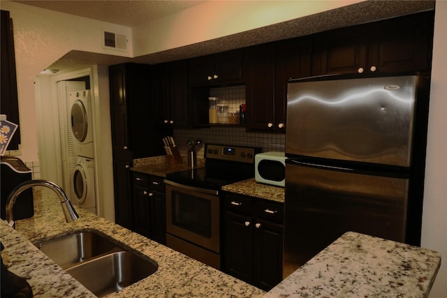 kitchen featuring stainless steel appliances, tasteful backsplash, stacked washer / dryer, light stone countertops, and sink