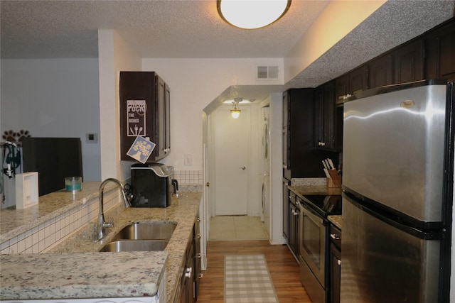 kitchen with appliances with stainless steel finishes, sink, light stone counters, and a textured ceiling