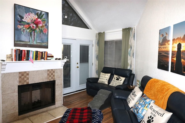 living room with a tiled fireplace, vaulted ceiling, and french doors