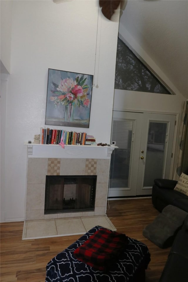 living room with vaulted ceiling, a fireplace, wood-type flooring, and french doors