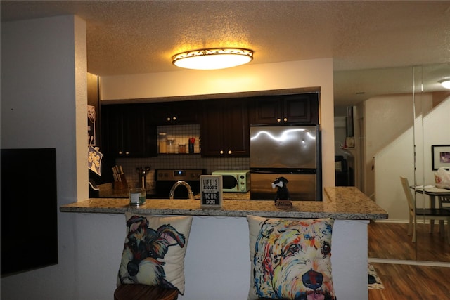 kitchen featuring backsplash, dark hardwood / wood-style floors, kitchen peninsula, stainless steel refrigerator, and light stone counters