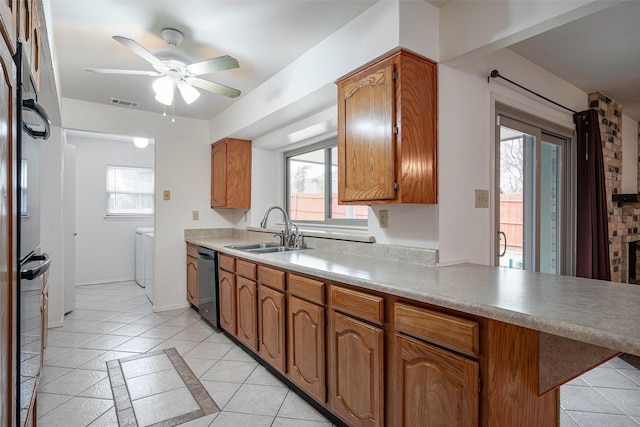 kitchen featuring washer and clothes dryer, dishwasher, brown cabinets, light countertops, and a sink