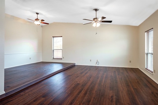 empty room featuring lofted ceiling, baseboards, dark wood finished floors, and a ceiling fan