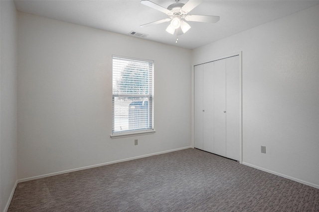 unfurnished bedroom with baseboards, visible vents, dark carpet, and a closet