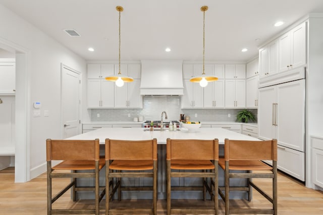 kitchen featuring white cabinets, paneled fridge, a center island with sink, and custom exhaust hood