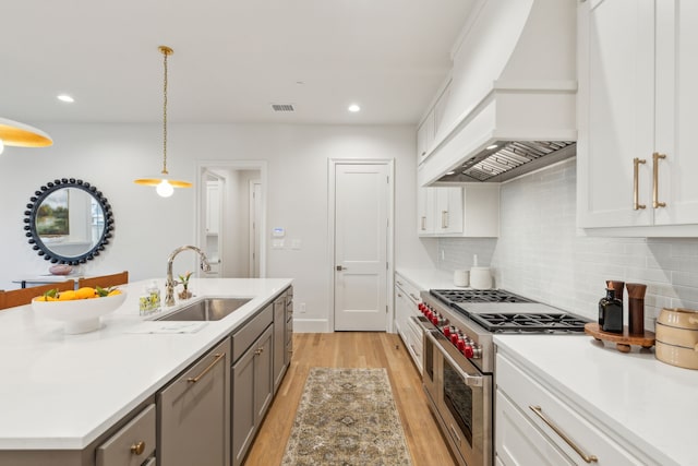 kitchen with white cabinets, stainless steel appliances, premium range hood, hanging light fixtures, and sink