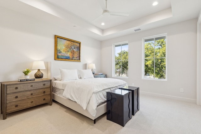 bedroom featuring ceiling fan, a tray ceiling, and light carpet